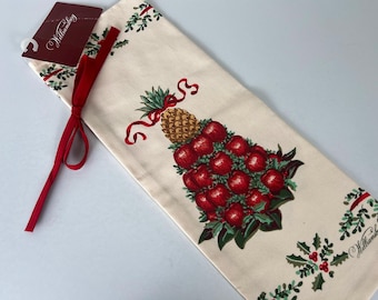 May include: Cream-colored kitchen towel with a Christmas tree design made of red apples and a pineapple. The towel has a red ribbon and a tag that says "Williamsburg". Green holly and red berries decorate the edges.
