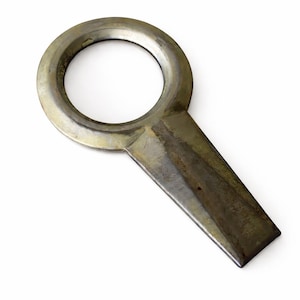 May include: A vintage metal bottle opener with a circular handle and a rectangular lever. The opener has a tarnished, aged appearance, with a dark, metallic finish. The design is simple and functional, suitable for opening bottles.
