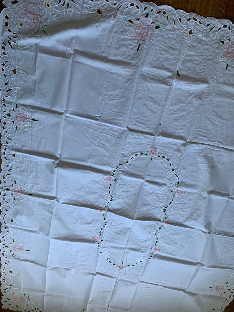 May include: White tablecloth with delicate floral embroidery and cut-out lace detailing. The embroidery features pink and green flowers.