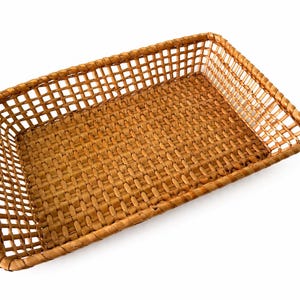 May include: A rectangular woven basket with a light brown finish. The base features a tight, solid weave pattern, while the sides are constructed with an open, grid-like lattice structure. The rim is reinforced with a thick, braided border.
