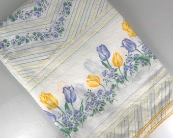 May include: White fabric with a yellow and green striped pattern. The fabric has a border of blue and purple flowers and yellow tulips.