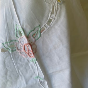 May include: White linen tablecloth with delicate embroidered floral designs in shades of pink, green, and yellow.