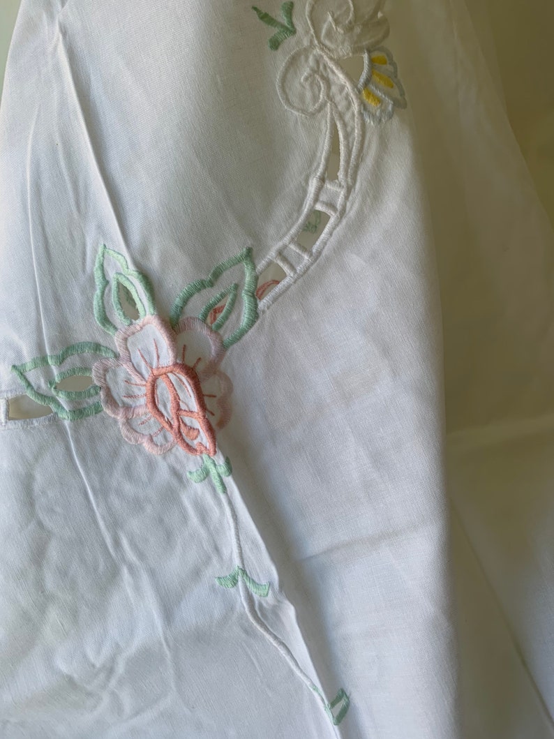May include: White linen tablecloth with delicate embroidered floral designs in shades of pink, green, and yellow.
