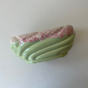 May include: A green and pink ceramic planter with a wavy design. The planter is made of glazed ceramic and has a smooth finish.