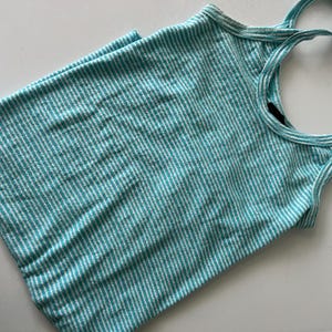Puede incluir: Camiseta sin mangas a rayas turquesa y blancas con tirantes finos. La parte superior est&aacute; hecha de una tela suave y acanalada. Los tirantes son de un tono m&aacute;s claro de turquesa y blanco.