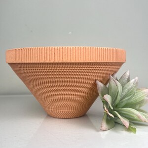 May include: A terracotta-colored ceramic planter with a textured, ribbed design. The planter is cone-shaped and has a wide, flat rim.