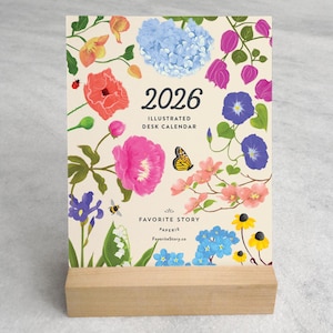 May include: A 2026 desk calendar with floral illustrations, including pink peonies, blue hydrangeas, and yellow butterflies. The calendar is displayed on a wooden stand. Text on the calendar reads "2026 Illustrated Desk Calendar" and "Favorite Story".