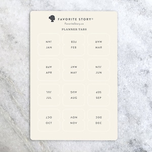 May include: A cream-colored planner tab sheet with the text "FAVORITE STORY" and "PLANNER TABS". Each tab is labeled with a month of the year, such as JAN, FEB, MAR, APR, MAY, JUN, JUL, AUG, SEP, OCT, NOV, and DEC.