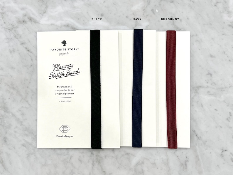 K&ouml;nnte beinhalten: Produktfoto von Planer-Gummib&auml;ndern in Schwarz, Marineblau und Burgunderrot. Jedes Band ist an einer wei&szlig;en Karte mit dem Text "Planner Stretch Band" und "7" flat loop befestigt. Der Markenname "Favorite Story" ist ebenfalls sichtbar.