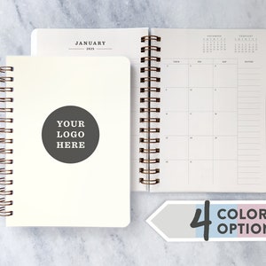 May include: A white spiral bound planner with a blank cover. The cover has a circle with the text "YOUR LOGO HERE". The planner has a calendar section with the months of December, January, and February. The planner is available in four colour options.