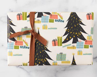 May include: White wrapping paper with a repeating pattern of black Christmas trees, colorful presents, and gold stars. A brown ribbon is tied around the paper.