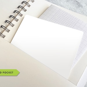 May include: Cream-colored spiral-bound notebook with a white pocket. The pocket contains a white card and a sheet of graph paper. The notebook is open, revealing the spiral binding and the pocket. The text "2-SIDED POCKET" is visible.
