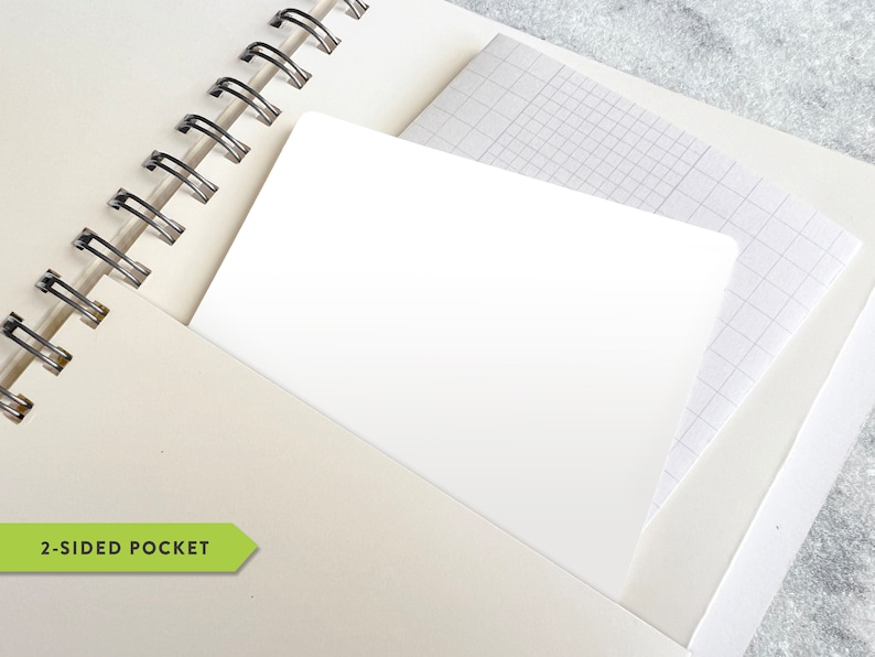 May include: Cream-colored spiral-bound notebook with a white pocket. The pocket contains a white card and a sheet of graph paper. The notebook is open, revealing the spiral binding and the pocket. The text "2-SIDED POCKET" is visible.