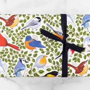 May include: Gift wrap featuring colorful illustrations of various birds, including cardinals, blue jays, and robins, set against a backdrop of green leaves. The paper is tied with a dark blue ribbon, creating a visually appealing package.