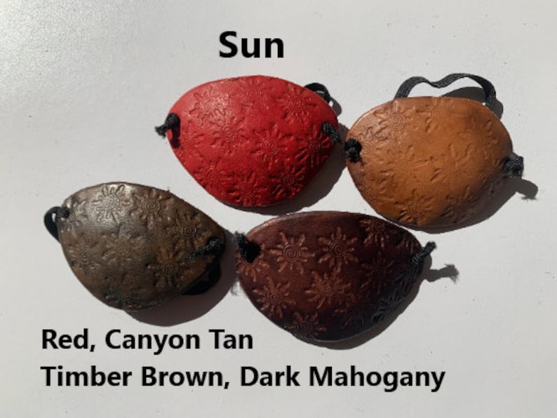 May include: Four leather eye patches in red, canyon tan, timber brown, and dark mahogany. Each patch has a sunburst design and a black elastic band. The word "Sun" is above the patches.