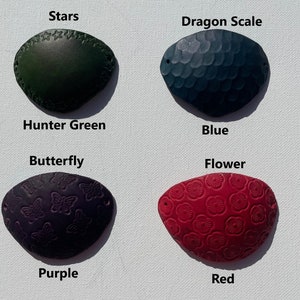 May include: Four leather eye patches in hunter green, blue, purple, and red. Each patch features a different embossed design: stars, dragon scales, butterflies, and flowers. The colors and designs are labeled below each patch.
