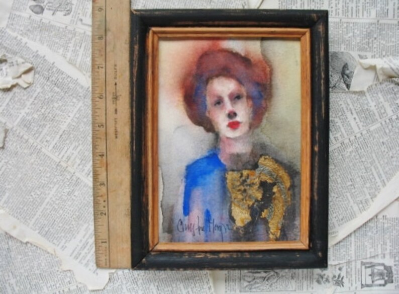 May include: A watercolor painting of a person with red hair and blue eyes wearing a blue shirt and a gold-colored scarf. The painting is framed in a black frame with a gold mat.