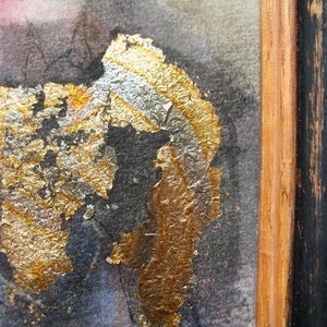 May include: Abstract art painting with gold and silver leaf accents on a dark background. The painting is framed in a black and wood frame.