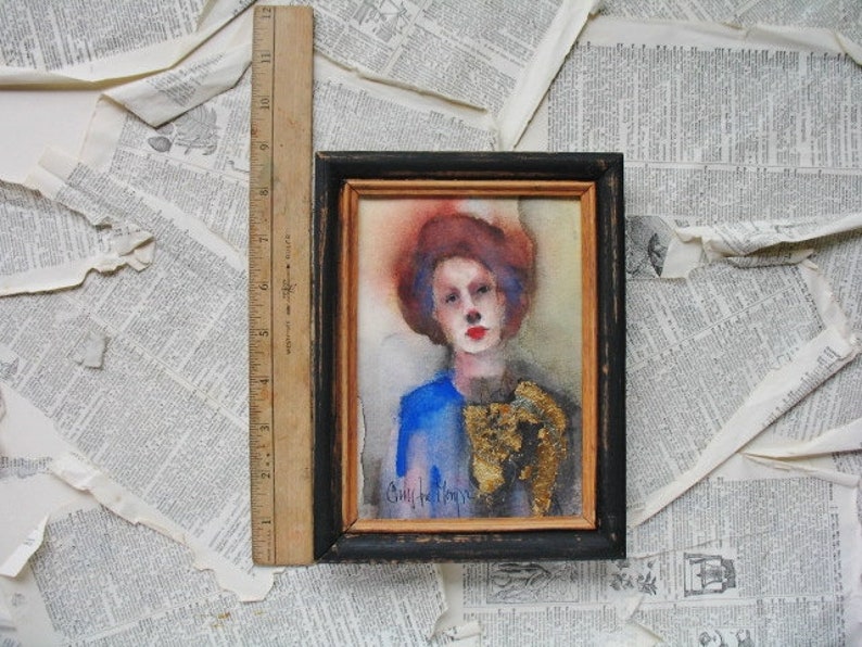 May include: A watercolor painting of a person with red hair wearing a blue and gold outfit. The painting is framed in black with a gold inner frame. The artist's signature is visible in the bottom left corner.
