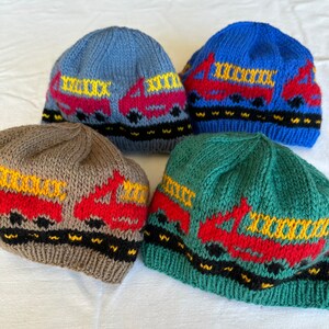May include: Four knitted hats in different colors with a red truck design. The hats are blue, brown, green, and light blue. Each hat has a yellow and black stripe around the bottom.