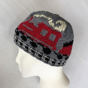 May include: A grey, red, black and white knitted hat with a geometric pattern. The hat is on a white mannequin head.