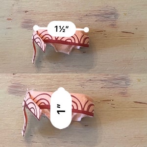 May include: Two pink fabric headbands with a red and white geometric pattern. The headband on top measures 1 1/2 inches wide and the headband on the bottom measures 1 inch wide.