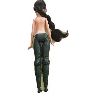 May include: A black doll with long black hair styled in a braid. The doll is wearing black trousers and boots.