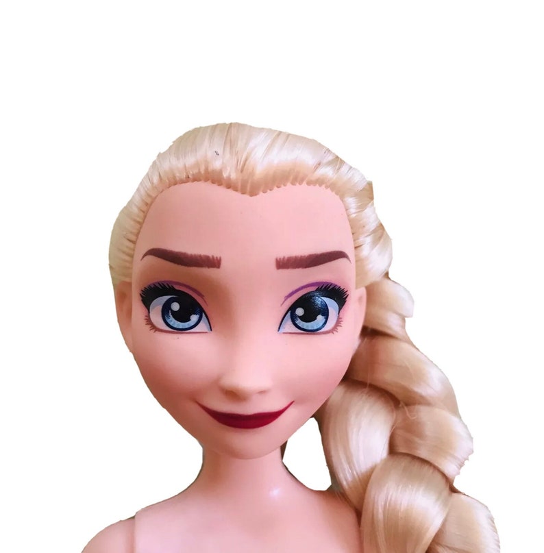 K&ouml;nnte beinhalten: Eine Puppe mit blonden Haaren, die zu einem Zopf geflochten sind, blauen Augen und einem gemalten L&auml;cheln. Die Puppe hat einen hellrosa Teint und tr&auml;gt keine Kleidung.