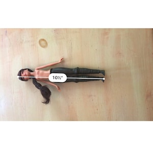 May include: A plastic doll with long black hair, wearing black trousers. The doll is 10 1/2 inches tall.