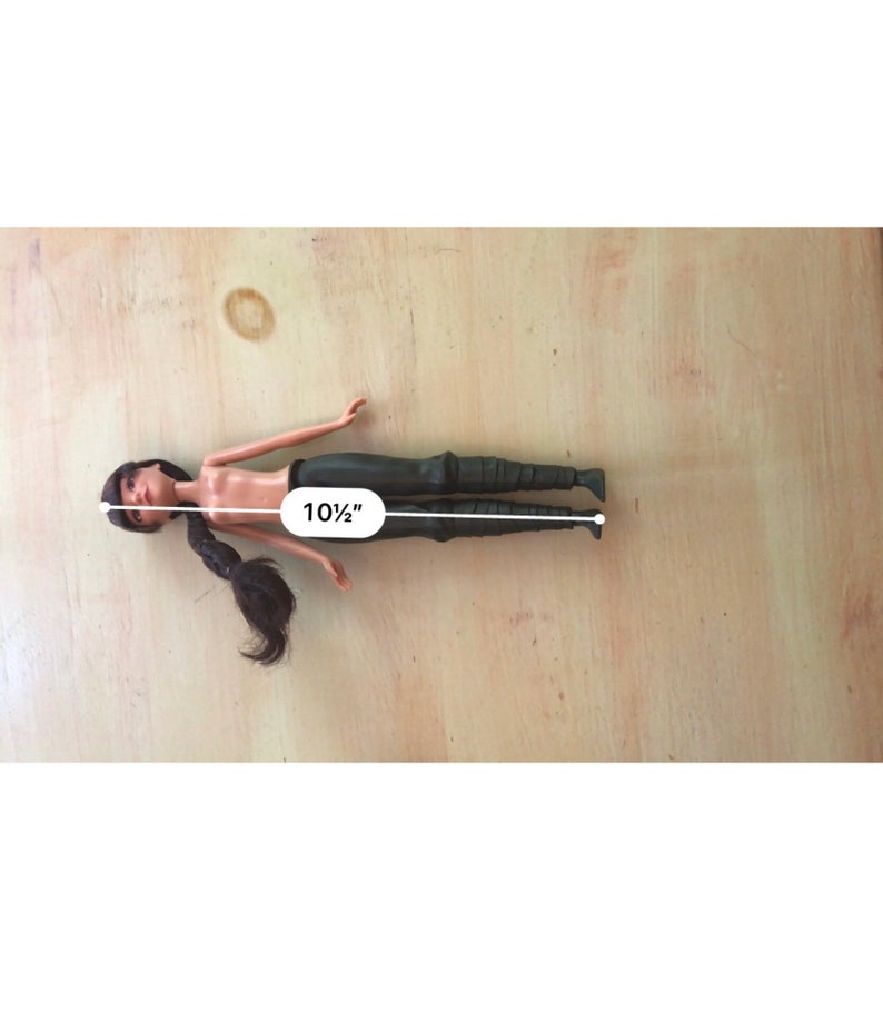 May include: A plastic doll with long black hair, wearing black trousers. The doll is 10 1/2 inches tall.