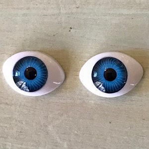 May include: Two blue plastic doll eyes with white sclera and black pupils. The eyes have a swirl pattern in the iris.