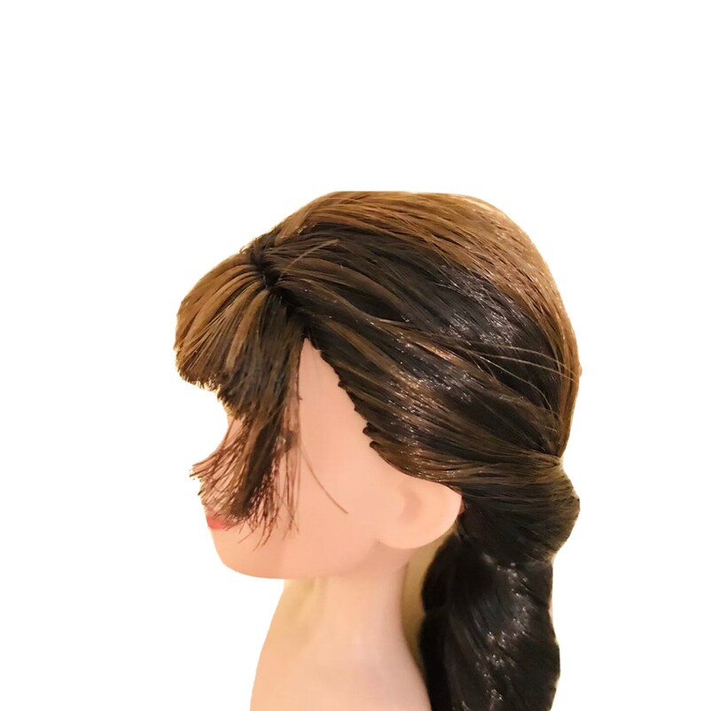 May include: A doll's head with long brown hair styled in a braid. The hair has highlights of a lighter brown colour.