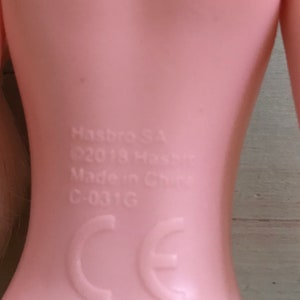K&ouml;nnte beinhalten: Nahaufnahme des R&uuml;ckens einer rosafarbenen Plastikpuppe mit dem aufgedruckten Text "Hasbro, &copy;2018 Hasbro, Made in China, C-031G, CE".
