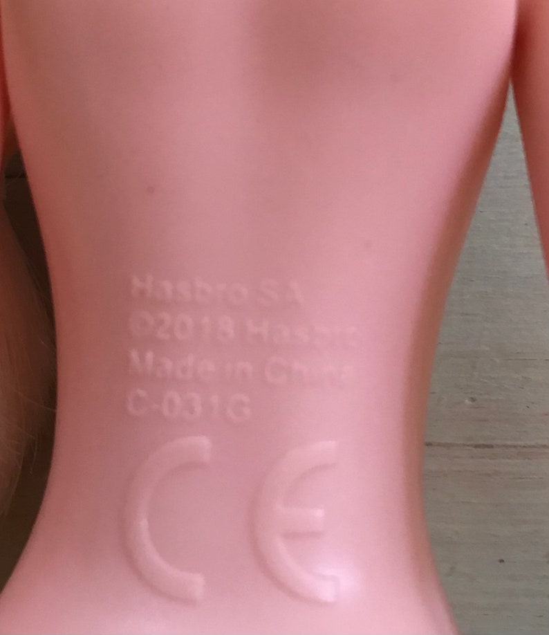 K&ouml;nnte beinhalten: Nahaufnahme des R&uuml;ckens einer rosafarbenen Plastikpuppe mit dem aufgedruckten Text "Hasbro, &copy;2018 Hasbro, Made in China, C-031G, CE".