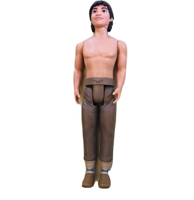 May include: A brown plastic doll with short black hair, wearing brown trousers and brown shoes. The doll has a sculpted face with brown eyes and a smile.