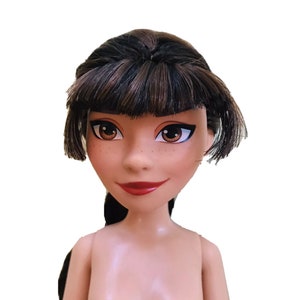 May include: A doll with brown hair styled in a bob with bangs. The doll has brown eyes and a light brown complexion. The doll is wearing no clothing.