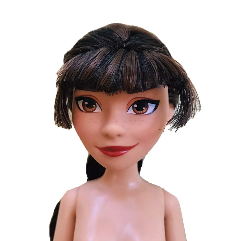 May include: A doll with brown hair styled in a bob with bangs. The doll has brown eyes and a light brown complexion. The doll is wearing no clothing.