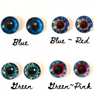 May include: A selection of glass doll eyes in different colours. The eyes are blue, blue and red, green, and green and pink. Each eye has a black pupil and is labelled with its colour.
