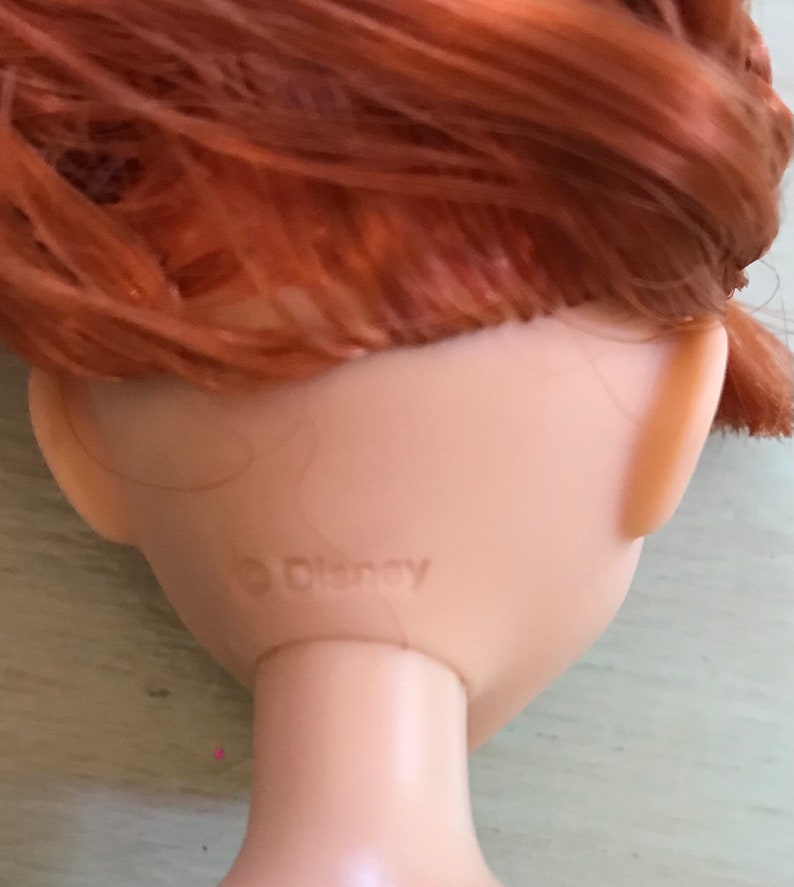 Puede incluir: Primer plano de la parte posterior de la cabeza de una mu&ntilde;eca con cabello rojo. La mu&ntilde;eca tiene un logotipo de Disney en la parte posterior del cuello.