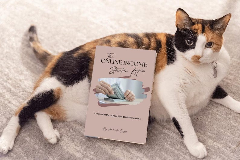 May include: A calico cat rests beside a book titled "The Online Income Starter Kit." The book cover is light pink with text and an image of hands holding money. The cat has a mix of black, orange, and white fur.
