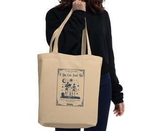 May include: A beige tote bag with a blue graphic of two skeletons holding hands under a crescent moon and stars. The text "If You Can Read This" is above the graphic. The text "It Means I'm Close To The One I Love Most" is below the graphic. The text "#Spooky" is at the bottom of the graphic.