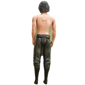Puede incluir: Una figura de acci&oacute;n de pl&aacute;stico marr&oacute;n de un hombre que lleva pantalones y botas negras. La figura tiene el pelo negro y el pecho desnudo. La figura tiene un c&oacute;digo de barras en la espalda que dice "#6041 62714".