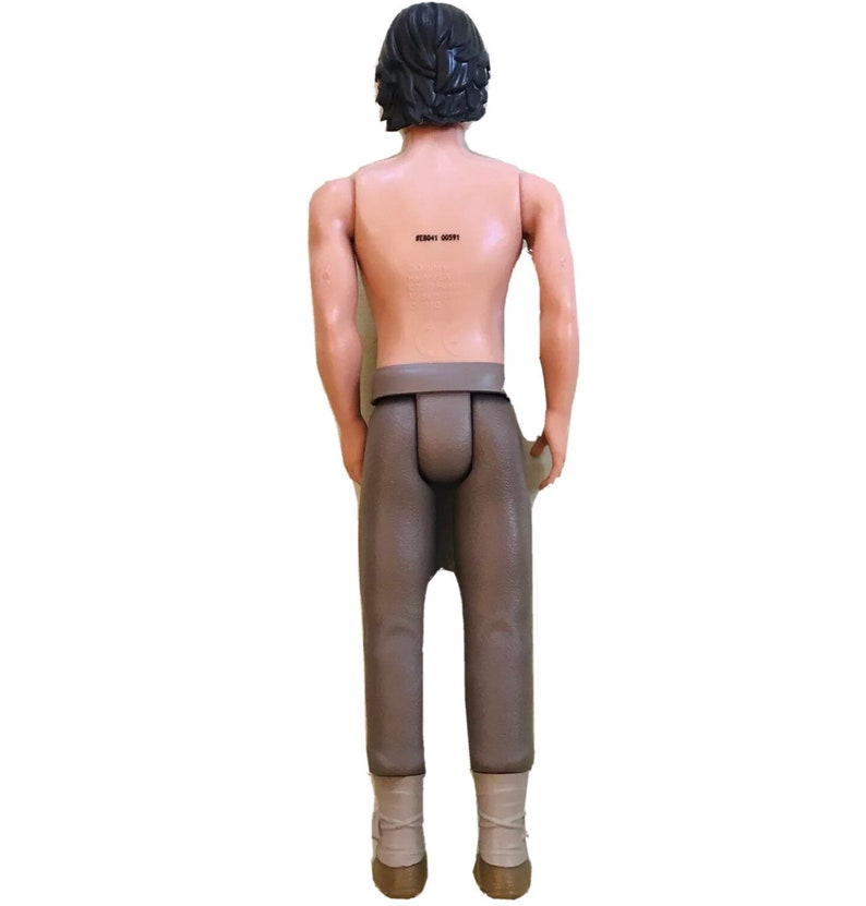 May include: A brown plastic action figure of a man with short black hair wearing brown trousers and brown boots. The figure has a barcode on its back.