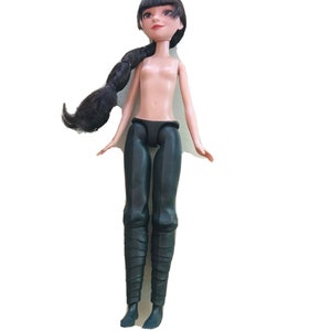 May include: A black-haired doll wearing a black outfit and black boots. The doll has a neutral expression and is looking upwards.