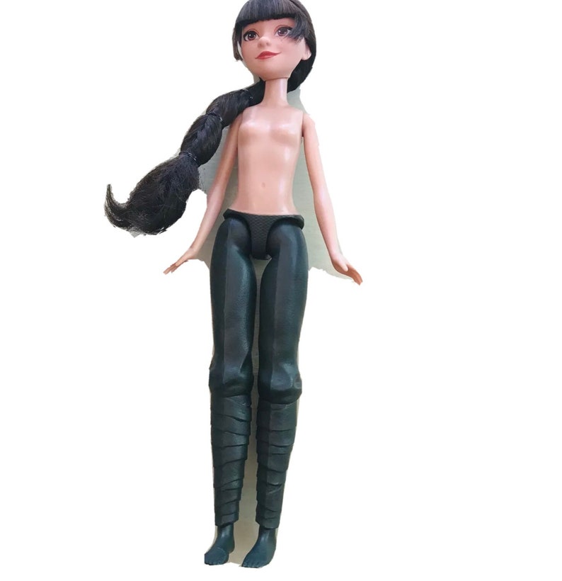 May include: A black-haired doll wearing a black outfit and black boots. The doll has a neutral expression and is looking upwards.