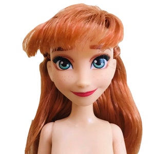 Puede incluir: Una cabeza de mu&ntilde;eca con cabello largo y rojo, ojos azules y una sonrisa rosa claro. La mu&ntilde;eca tiene pecas y no lleva ropa.
