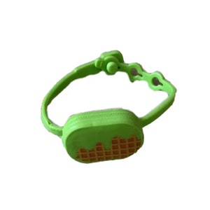 May include: A green plastic fanny pack with a waffle design and green icing. The fanny pack has a buckle closure.