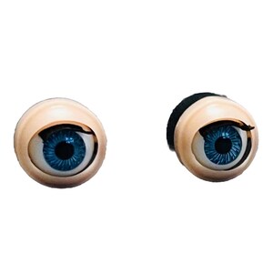 May include: Two doll eyes with blue irises and a light skin tone. The eyes have a realistic appearance with detailed iris patterns and black eyelashes. One eye has a black backing.