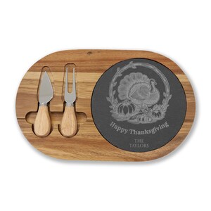 Può includere: Tagliere in legno con inserto in ardesia. Include un coltello e una forchetta per formaggio con manici in legno. L'inserto in ardesia presenta un disegno di tacchino del Ringraziamento e il testo "Happy Thanksgiving" e "The Taylors".