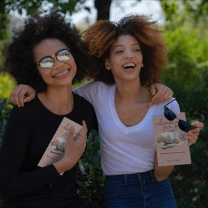May include: Two smiling people, one in a black long-sleeve shirt and the other in a white V-neck, hold books with the title "The Online Incubation Guide". Both wear sunglasses. The background is a blurred outdoor scene.